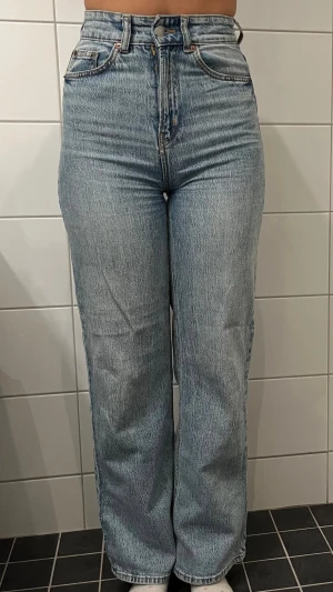 Blå raka jeans med hög midja - Säljer ett par klassiska blå jeans med rak passform och hög midja. Jeansen har fem fickor, dragkedjegylf och är tillverkade i ett slitstarkt denimtyg. Perfekta för en avslappnad och trendig look.