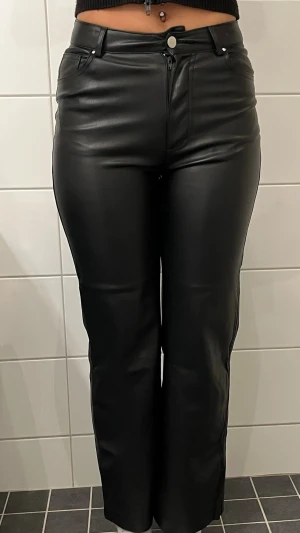 Svarta skinnbyxor med raka ben - Snygga svarta skinnbyxor med raka ben och hög midja. Byxorna har två bakfickor och en stilren look som passar till många olika outfits. Tillverkade i mjukt skinnmaterial som ger en cool vibe.