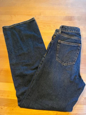 Mörkblå raka jeans med hög midja - Säljer ett par klassiska mörkblå jeans med raka ben och hög midja. Jeansen har fem fickor, bälteshällor och kontrastsömmar. Perfekta till en avslappnad och stilren look. Materialet är kraftig denim i bomull. De bästa jeansen till en fin middag!