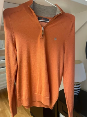 Orange ziptröja från Morris - Snygg orange långärmad tröja från Morris med halv dragkedja och liten broderad logga på bröstet. Tröjan har ribbade muddar och krage i kontrastfärg på insidan. Perfekt för dig som gillar stilrena plagg med en twist. Storlek XS