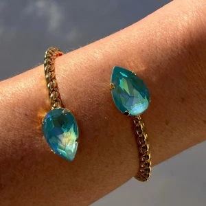  Armband Bangle Summer Blue De Lite - Armband, Bangle, i guldpläterad mässing med kristaller. Kristaller Pear 18mm. Färg Summer Blue De Lite, ställbar storlek. Egen design. Jag skickar endast spårbart, samfraktar. Fast pris. Besök gärna mina övriga annonser.  Till mina smycken använder jag kristaller från Preciosa, Aurora och Swarowski.