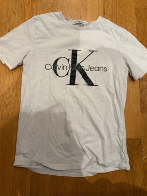 Vit Calvin Klein Jeans t-shirt - Snygg vit t-shirt från Calvin Klein Jeans med stor svart CK-logga och text på bröstet. Klassisk rund halsringning och korta ärmar. Tillverkad i mjuk bomull som känns skön mot huden. Perfekt för en clean och stilren look.