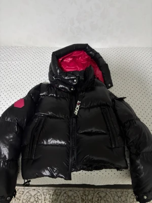 Svart dunjacka från Jack1t - Snygg svart dunjacka från Jack1t med glansig finish och rosa innerfoder. Jag köpte jackan för ungefär 2500 nypris och säljer den för detta priset. Vid snabbköp var gärna säkra och prisförslag är alltid välkomna 