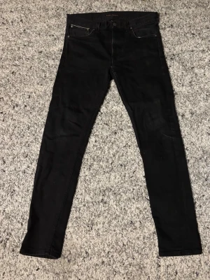 Svarta  Selvedge jeans från Nudie  - Svarta skinny jeans från Nudie med klassisk femficksdesign och smal passform. Jeansen har diskreta sömmar och är tillverkade i stretchigt denimtyg för en bekväm känsla. Perfekta för en stilren och modern look.