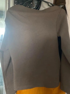 Brun offshoulder topp - Säljer en brun offshoulder topp med lång ärm. Toppen har en enkel och stilren design med rak passform och är tillverkad i ett mjukt material som känns skönt mot huden. Perfekt för dig som gillar minimalistisk stil.