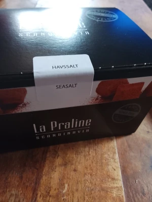 Presentbox med praliner och te - En snygg presentbox från La Praline Scandinavia med havssaltpraliner och två sorters svart te från Kaffekassan: Masala Chai och Sweet Peppermint. Förpackningen är svart med vita detaljer och innehållet passar perfekt för en mysig fikastund.