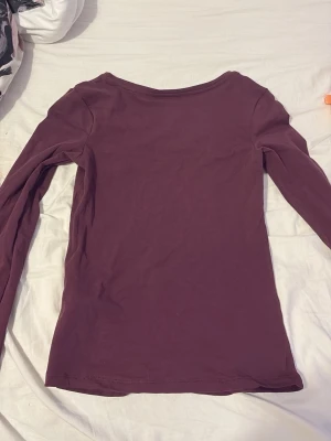 Vinröd långärmad topp från 157 - En enkel och stilren långärmad topp i mörkröd/lila från 157. Modellen har rund halsringning och är tillverkad i mjukt, stretchigt material som sitter skönt mot kroppen. Perfekt att matcha med jeans eller kjol för en avslappnad look.