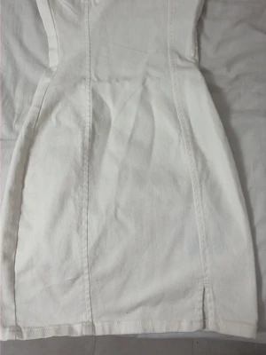 Vit figurnära kort klänning - Säljer en vit, figurnära kort klänning i kraftigt bomullstyg. Klänningen har markerade sömmar som framhäver midjan och en dragkedja i sidan för enkel påklädning. Enkel och stilren design som passar perfekt till sommaren.