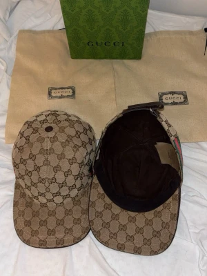  keps - Säljer en beige keps i klassiskt GG canvasmönster. Kepsen har böjd skärm, justerbart spänne bak och detaljer i brunt. Ikonisk design med gröna och röda ränder på sidan. Perfekt accessoar för dig som gillar lyxig streetwear.