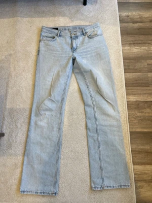 Ljusblå raka jeans - Säljer ett par ljusblå jeans med rak passform och klassisk femficksdesign. Jeansen har normal midja och är tillverkade i denim med tydliga sömmar. Perfekta för en avslappnad och trendig look.
