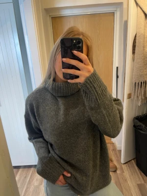 Grå polotröja i ullmix - Mysig grå stickad polotröja med oversized passform och breda ribbade muddar vid ärmslut och hals. Perfekt för kalla dagar och enkel att styla med jeans eller kjol. Materialet känns mjukt och värmande.