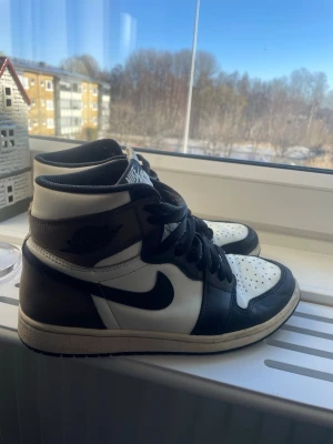 Nike Air Jordan 1 mocka High svart/vit/ brun - Säljer ett par Nike Air Jordan 1 High sneakers i svart och vitt med klassisk Swoosh på sidan. Super fina Jordan mocka, köpta för 6000kr