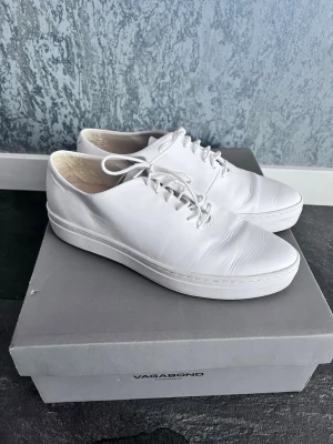 Vita sneakers från Vagabond - Stilrena vita sneakers från Vagabond med klassisk låg profil och snörning. Skorna är tillverkade i slätt läder och har en tjock vit sula som ger en modern look. Perfekta för dig som gillar minimalistisk och clean stil.