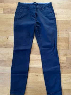 Mörkblå chinos  - Snygga mörkblå chinos med smal passform och klassiska fickor fram och bak. Byxorna har bälteshällor och stängs med knapp och dragkedja. Perfekta för en clean och stilren look. Materialet känns mjukt och följsamt, troligen bomull med lite stretch.