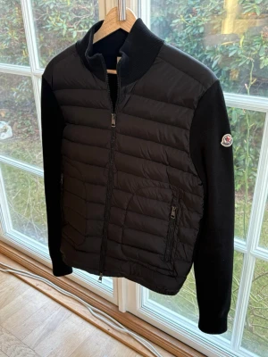 Moncler Cardigan - Snygg svart cardiganjacka från Moncler med quiltad front och stickade ärmar i nytt skick. Jackan har dragkedja framtill, två sidofickor med dragkedja och Moncler-logga på ärmen. NFC Scan fungerar. Pris kan diskuteras.