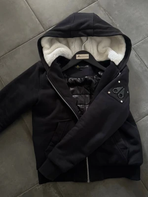 Moose Knuckelers hoodie/jacka - Säljer en Moose Knucklers hoodie som är fodrad i storlek L Barn vilket motsvarar någon som är 156-166 cm. Den har stor huva och mjukt vitt teddyfoder i. Passar perfekt till våren eller kallar sommar dagar(Pris går att diskutera vid snabb affär)