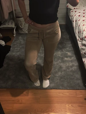 Beiga Juicy Couture byxor  - Snygga Juicy Couture byxor i beige imjuk velour med raka ben och bred resår i midjan. Byxorna har dekorativ knytning framtill och bakfickor med guldfärgade knappar. Perfekta för en chill och avslappnad stil. Lite sletet på slutet av byxan (se sista bilden) annars inga problem. 