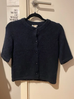 Mörkblå stickad kofta Gina Tricot - Mysig mörkblå stickad kofta från Gina Tricot med korta ärmar och rund hals. Koftan har knappar framtill och en croppad passform som ger en trendig look. Perfekt att styla över ett linne eller t-shirt. Följer med en extra knapp. Skickar helst med PostNord😊