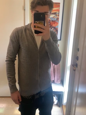 Grå ziptröja i tunn bomull - Säljer en stilren grå ziptröja med lång ärm och dragkedja framtill. Tröjan är tillverkad i tunn bomull och har en enkel, clean look som passar perfekt till jeans eller över en t-shirt. Perfekt för lager på lager och chill vardagsstil. Priset är ej ristat i en sten. Den är i storlek M men passar L också.