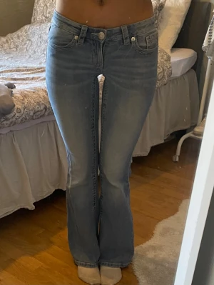 Ljusblå bootcut jeans med brodyr - Säljer ett par ljusblå bootcut jeans med snygg brodyr på bakfickorna. Jeansen har låg midja, klassisk femficksmodell och är tillverkade i denim. Perfekta för dig som gillar en avslappnad men trendig stil.