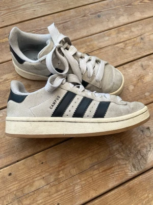 Adidas Campus skor  - Beiga och Svarta adidas campus skor. Ett par andvända skor med vissa skavanker men fortfarande fina! Dem har ett hål i en hälen😊 Storlek 37 1/3