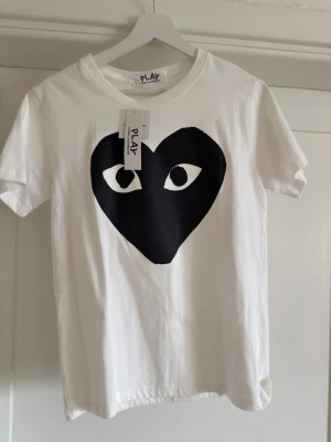 Vit t-shirt från Comme des Garçons Play - Vit t-shirt från Comme des Garçons Play. Klassisk rund halsringning och korta ärmar. Materialet är mjuk bomull och passformen är som normal, kanske lite närmare xs.