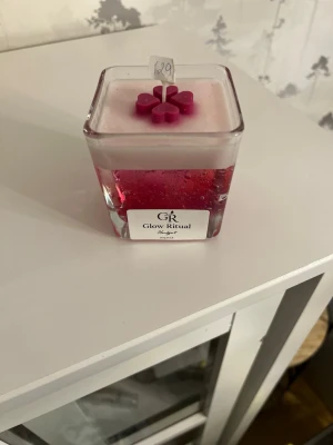 Doftljus i glas - Fyrkantigt handgjord doftljus i glasbehållare. Ljuset är rosa och vitt med hjärtor på toppen. Perfekt som inredningsdetalj eller present. 