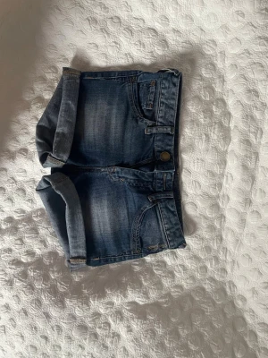 2000s low waist jeansshorts  - Snygga blå jeansshorts med uppvikta ben och klassisk femficksdesign. Shortsen har knapp och dragkedja framtill samt bälteshällor. Perfekta för varma dagar och ger en avslappnad 2000s look!