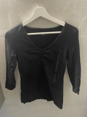 Svart v-ringad topp med trekvartsärm - Stilren svart topp med v-ringning och trekvartsärm. Snygg passform och enkel design som passar till mycket. Tillverkad i ett mjukt material.