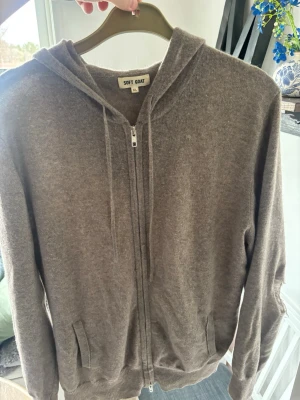 Brun hoodie med dragkedja från Soft Goat - Mjuk och lyxig brun hoodie från Soft Goat i storlek XL. Men passar inte XL utan L. Tillverkad i kashmir med dragkedja framtill, två fickor och ribbade muddar. Huva med snören för justering. Perfekt för dig som gillar stilren och bekväm design. Ändå felet är hålet på ena armen på bild 3. Det kan man lösa med en snygg armlapp tex!