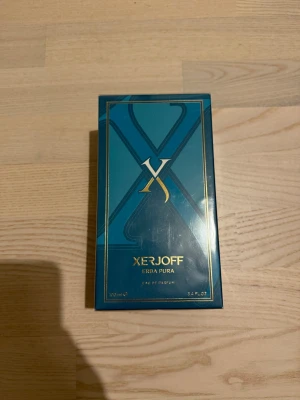 Xerjoff Erba Pura Eau de Parfum - Exklusiv parfym från Xerjoff, Erba Pura, i en elegant blå och guld kartong. Förpackningen har en lyxig design med stora X-detaljer och guldtext. Perfekt för dig som vill ha något unikt och stilrent i parfymhyllan.