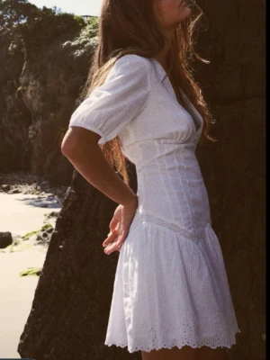 Vit kort klänning från Zara - Superfin vit kort klänning från Zara med v-ringning, puffärm och volangkant nertill. Klänningen har broderade detaljer och är tillverkad i ett lätt bomullstyg som passar perfekt till varma dagar. Söt och feminin modell med markerad midja. Passar perfekt till studenten och den är helt ny!