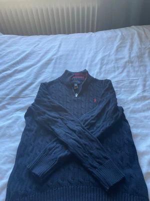Mörkblå kabelstickad tröja Polo - Mörkblå stickad tröja från Polo Ralph Lauren med halvzip och ribbade muddar. Inga tecken på slitning eller användning. Storlek är L/G så passar dig som har S eller M i tröjor. ( ny pris 1800)