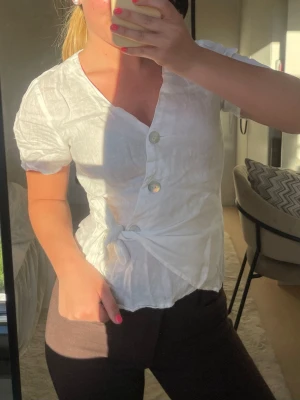 Vit asymmetrisk blus med knappar🩵 - Säljer en vit blus med korta ärmar och asymmetrisk knäppning framtill. Blusen har tre stora pärlemorknappar och lätt skrynkligt tyg som ger en avslappnad look. Passar perfekt till både jeans och kjol för en trendig stil.