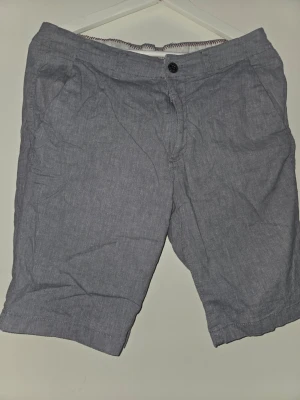 Gråa shorts med knapp - Säljer ett par grå shorts med klassisk passform och midwaist. De har fickor fram och bak samt stängs med knapp och dragkedja. Perfekta för varma dagar och enkel stil. Passar dig som gillar en clean look.