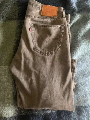 Levi's 501 bruna jeans W33 L32 - Säljer ett par klassiska Levi's 501 jeans i brun färg. Modellen har rak passform, fem fickor och den ikoniska läderpatchen bak i midjan. Jeansen är tillverkade i bomull och har den typiska röda Levi's-taggen på bakfickan.