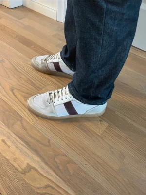 Vita Ami Paris sneakers med gummisula Storlek 43 - Snygga vita sneakers från Ami med beige och bruna detaljer. Skorna har en klassisk låg siluett och en slitstark gummisula. Insidan är mjuk och bekväm, perfekt för dig som gillar stilrena och tidlösa sneakers. Kolla alla bilder för skavanker och bedöm skick. Pris kan diskuteras, hör av dig!