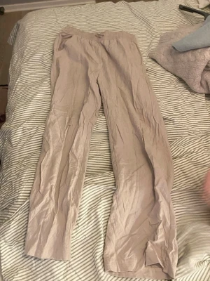Beige linnebyxor med resårmidja - Säljer ett par beige linnebyxor med avslappnad passform och resår i midjan. Byxorna har raka ben och sidofickor, perfekta för en chill och stilren look. Materialet är lätt och luftigt, vilket gör dem sköna att bära under varma dagar.