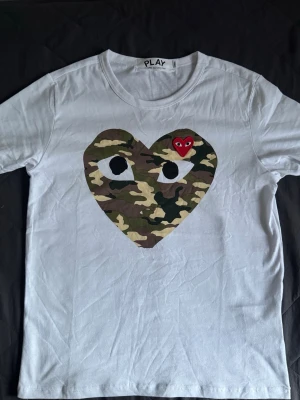 Comme des Garçons Play camo t-shirt - Vit t-shirt från Comme des Garçons Play med stort hjärta i camouflage-mönster. Storleken är S och passformen är slim/regular och sitter fint. Kom dm för fler bilder och om ni har frågor..