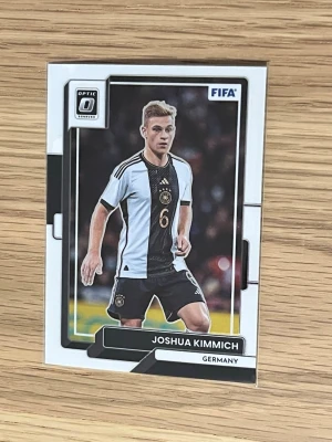 FIFA samlarkort Joshua Kimmich - Samlarkort från Panini Optic med Joshua Kimmich i Tysklands landslagströja. Kortet har svartvita detaljer och visar spelaren i matchställ. Perfekt för dig som gillar fotboll och samlar på sportkort.