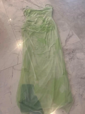 Ljusgrön långklänning med snörning - Trendig ljusgrön långklänning med tunna axelband och snygg snörningsdetalj i sidan. Klänningen har en lätt transparent look och är figurnära med en mjuk, följsam passform. Perfekt för sommarens alla tillfällen.