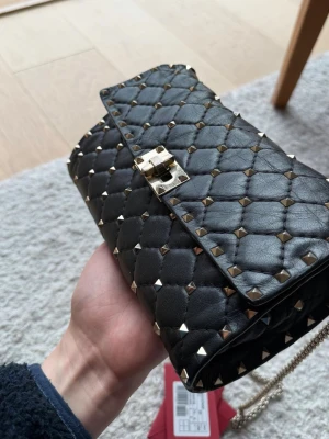 Valentino Garvani Rockstud   - Valentino Garavani Rockstud Spike chain crossbody bag in supple lambskin nappa. Quilted construction enriched with small studs. Equipped with a detachable chain strap, this accessory can be worn as a crossbody/shoulder bag or carried by hand.  - Quilted nappa. Rhombus pattern enhanced by tone-on-tone stitching  - Platinum-finish metal studs and hardware Flap with twist-lock closure  - Nappa lining. Interior: red leather zip pocket and 8 card slots  - Dimensions: W23xH13.5xD4.5 cm  - Made in Ital