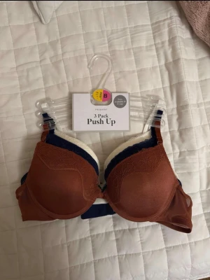 3-pack push up bhar från Primark - Säljer ett 3-pack push up bhar från Primark i färgerna rostbrun, marinblå och vit. Alla bhar har spetsdetaljer upptill och justerbara axelband. Perfekt för dig som vill ha både komfort och snygg form. Helt nya utan etikett, men med original förpackning. Säljes för att dem var för små. Deras storlek är 80B men passar mer för 70-75B. Priset kan diskuteras 