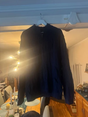 Mörkblå kabelstickad tröja - Mysig mörkblå kabelstickad tröja med rund hals och långa ärmar. Tröjan har klassiskt stickat mönster och ribbade muddar vid ärmslut och nederkant. Perfekt för lager-på-lager och en stilren look.