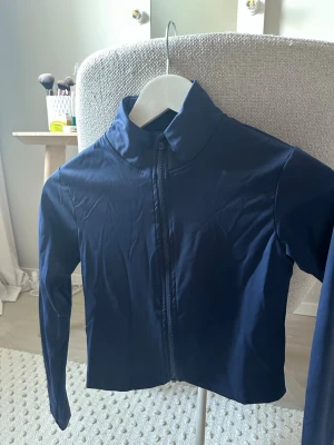 Mörkblått träningsset med jacka och tights - Snyggt mörkblått träningsset med långärmad jacka med dragkedja och matchande höga tights. Setet är gjort i ett stretchigt och mjukt funktionsmaterial som passar perfekt till träning. Diskret logga på tightsen. Perfekt för gymmet eller löprundan.