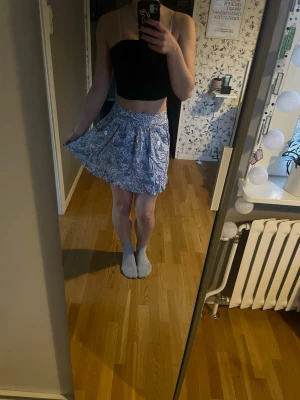 Blåvit kortkjol med paisleymönster - Säljer en blåvit kortkjol med paisleymönster. Kjolen har en luftig och lätt form med resår i midjan som gör den enkel att bära. Perfekt för varma dagar och ger en avslappnad vibe. Materialet känns mjukt och bekvämt mot huden. Har ett litet hål i ena fickan av kjolen. Lätt att sy ihop