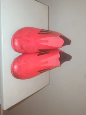 Rosa Adidas fotbollsskor utan snörning - Säljer ett par rosa Adidas fotbollsskor utan snörning med svarta detaljer och dobbar för spel på gräs. Skorna har en strömlinjeformad design och är tillverkade i syntetmaterial för bra grepp och känsla på planen.