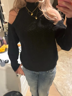 Svart stickad tröja med cold shoulder - Trendig svart stickad tröja med cold shoulder-detaljer och hög hals. Mjukt material och långärmad modell som passar perfekt till jeans eller kjol. Snygg strukturstickning ger extra stilpoäng.