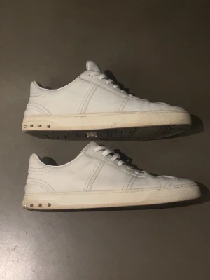 Vita Valentino flycrews  - Säljer ett par stilrena vita sneakers från Valentino med klassisk låg profil och coola nitar på sulan. Skorna är i läder med vita snören och diskreta sömmar som ger en clean look. Perfekta för dig som gillar exklusiva och trendiga sneakers.