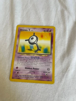 Pokémonkort Unown (M) 41/64 - Unikt Pokémonkort med Unown (M) från Neo Discovery-serien, nummer 41/64. Kortet har lila och gul ram, klassisk Pokémon-design och motiv av Unown mot färgglad bakgrund. Perfekt för samlare eller Pokémonfans som vill utöka sin kortsamling.